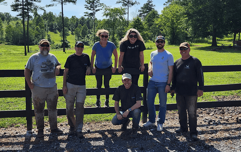 Seven Nexus Circular team members posing along a wooden fence in a green field